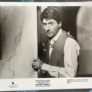 以下が含まれることがあります： ストライプのシャツとベストを着た男性の白黒写真。写真の最下部には「TOM CONTI stars as Stuart, an obsessive therapist who is more neurotic than his own patients.」というテキストがあります。