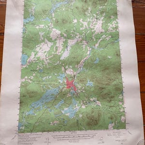 May include: A United States Geological Survey topographic map of the Saranac Lake region in New York. The map features green forested areas, blue bodies of water, and red urban zones, with detailed contour lines and geographic labels.