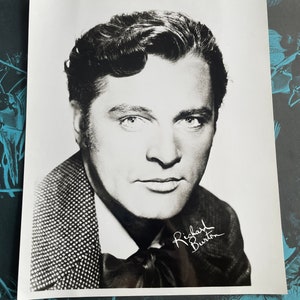 May include: Black and white photograph of Richard Burton, a renowned actor, with his autograph.