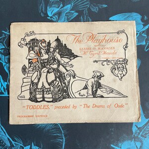Puede incluir: Un programa de teatro vintage para una representación de "TODDLES" precedida de "The Drums of Oude". El programa presenta una ilustración en blanco y negro de una pareja en un escenario teatral. El programa está impreso en papel crema con texto marrón.