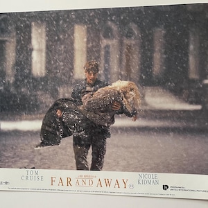 以下が含まれることがあります： 映画「Far and Away」のスチール写真。トム・クルーズが雪の降る通りでニコール・キッドマンを抱きかかえている。映画のタイトルと俳優の名前が表示されている。ヴィンテージのプロモーションアイテム。