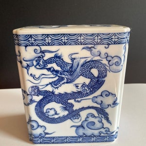 May include: A white ceramic rectangular box with a blue and white dragon design. The dragon is depicted in a swirling pattern with clouds and a blue border.