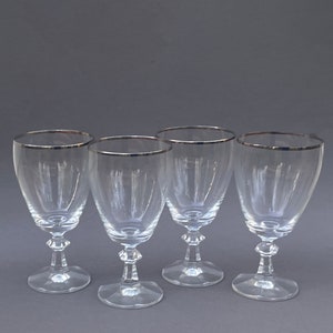 May include: Set of four clear glass wine glasses with a silver rim.