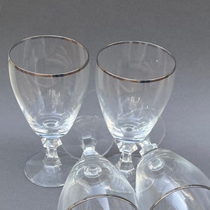 May include: Four clear glass wine glasses with a silver rim. The glasses are stacked on top of each other.
