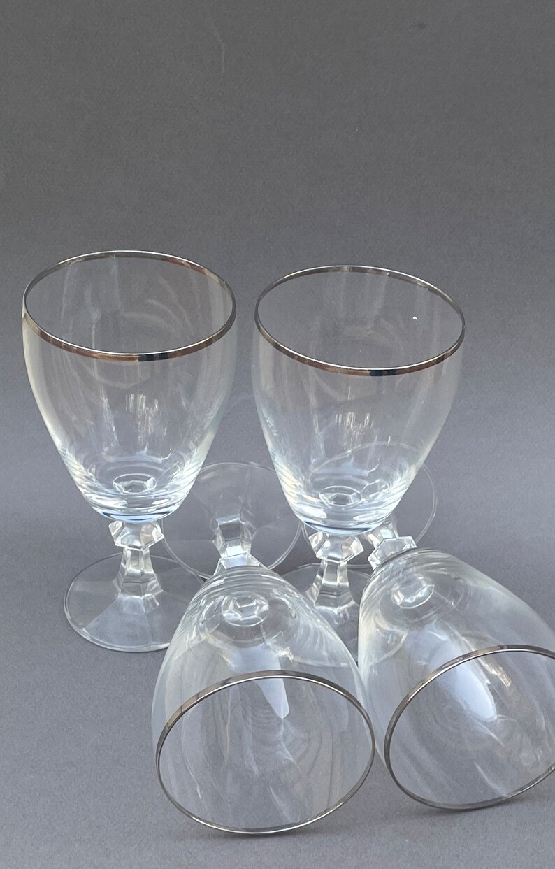 May include: Four clear glass wine glasses with a silver rim. The glasses are stacked on top of each other.