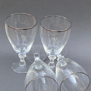 May include: Four clear glass wine glasses with a silver rim. The glasses are stacked on top of each other.