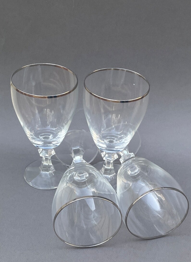 May include: Four clear glass wine glasses with a silver rim. The glasses are stacked on top of each other.