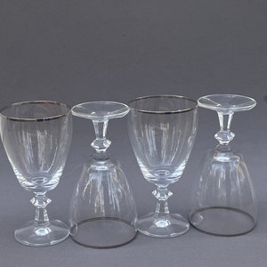 May include: Four clear glass wine glasses with silver rims. The glasses are arranged in a row on a gray surface.