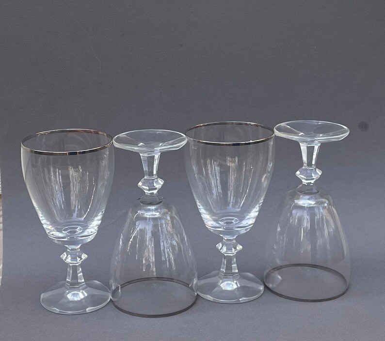 May include: Four clear glass wine glasses with silver rims. The glasses are arranged in a row on a gray surface.