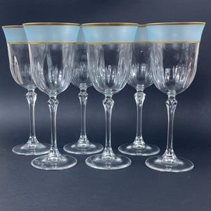 May include: Set of six clear glass wine glasses with a light blue and gold band around the top of each glass.