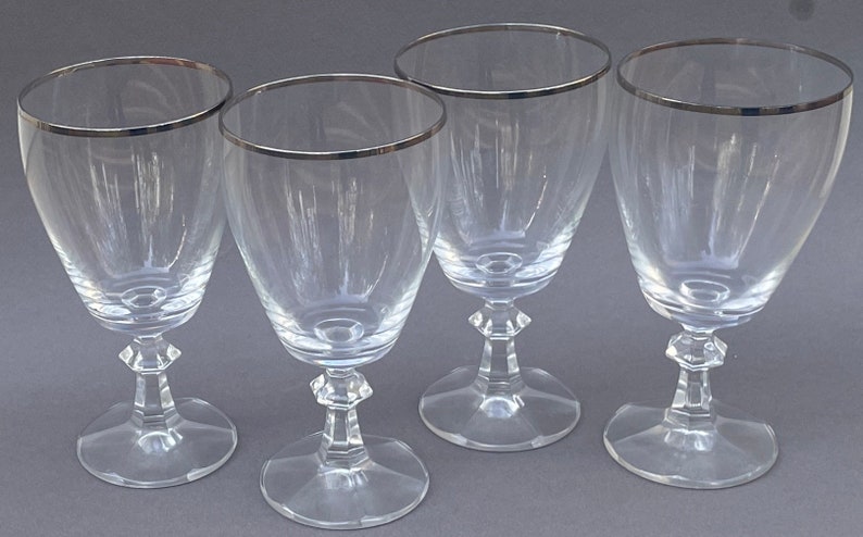 May include: Four clear glass wine glasses with a silver rim. The glasses have a tall, slender stem and a round bowl.