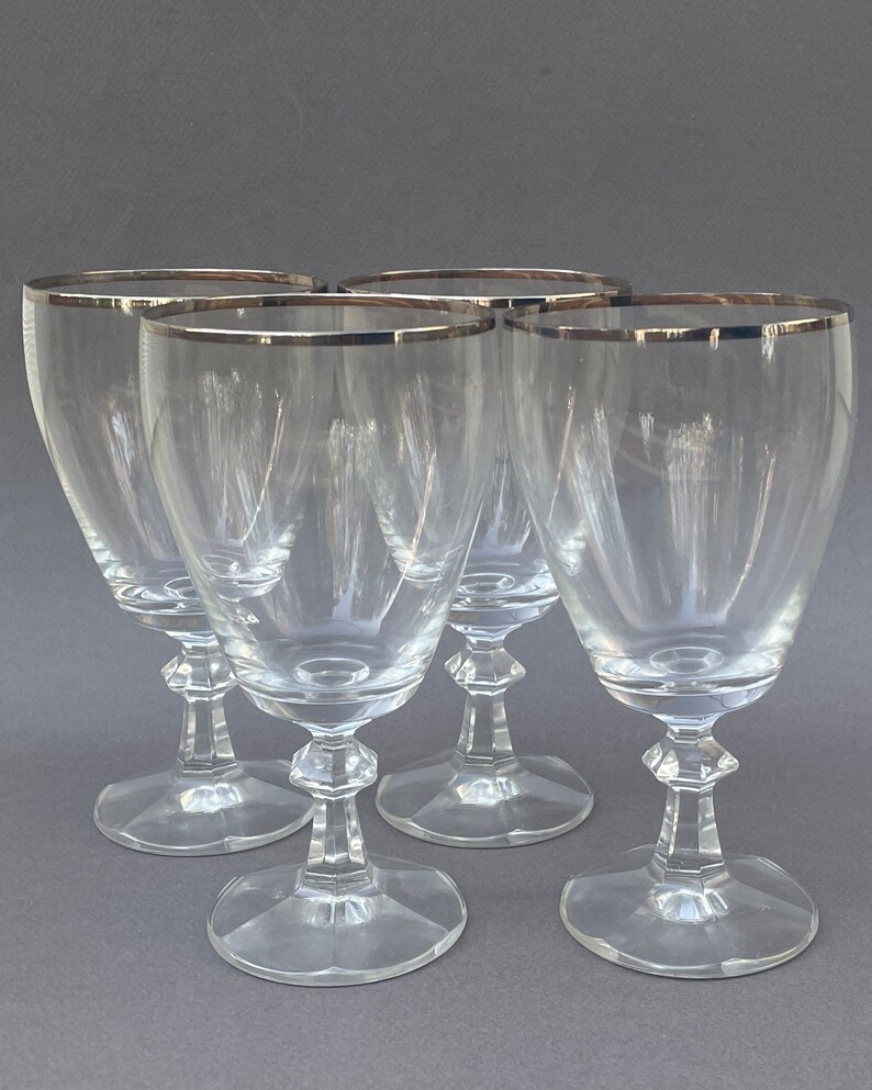 May include: Set of four clear glass wine glasses with a silver rim. The glasses have a classic design with a tall, slender bowl and a short stem.