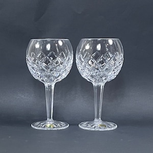 May include: Two clear crystal wine glasses with a cut diamond pattern. The glasses have a round bowl and a long stem.