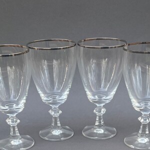 May include: Set of four clear glass wine glasses with a silver rim.