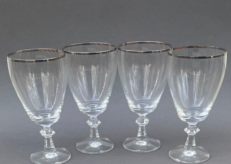 May include: Set of four clear glass wine glasses with a silver rim.