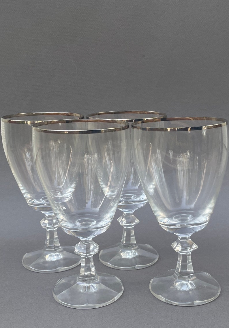 May include: Set of four clear glass wine glasses with a silver rim. The glasses have a classic design with a tall, slender bowl and a short stem.