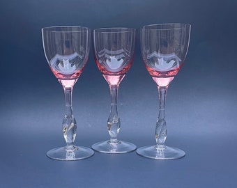 May include: Three clear glass wine glasses with a pink tint at the bottom. The glasses have a twisted stem and a round bowl.