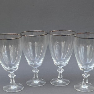 May include: Four clear glass wine glasses with silver rims. The glasses have a traditional shape with a wide bowl and a long stem.
