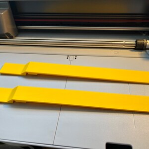 May include: Two yellow plastic cutting mats for a craft cutter. The mats are on a gray surface.