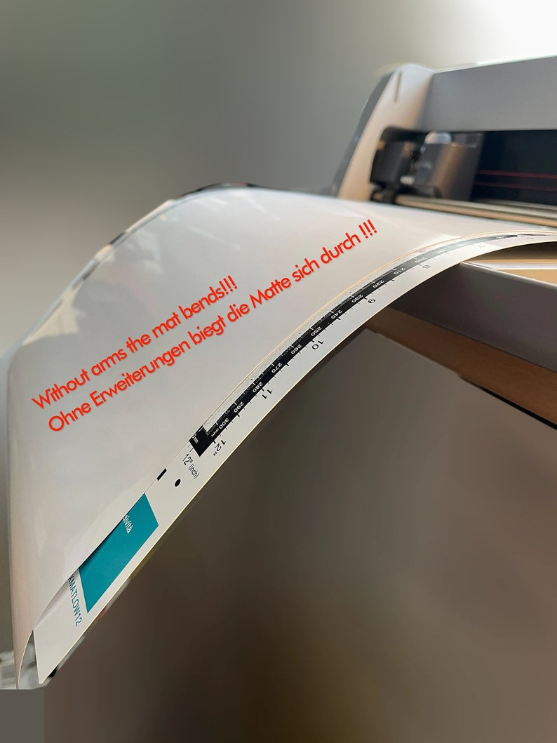 May include: A white cutting mat is being fed into a cutting machine. The mat is bending and the text "Without arms the mat bends!!! Ohne Erweiterungen biegt die Matte sich durch!!!" is visible on the mat.