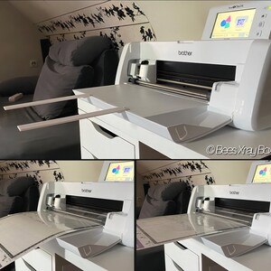 May include: A white Brother ScanNCut DX die-cutting machine with a white cutting mat and a white cutting blade. The machine has a touchscreen display with a colorful graphic of geometric shapes. The machine is on a white desk with a white drawer.