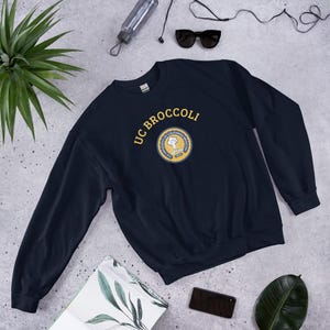 May include: A navy blue sweatshirt with the text "UC BROCCOLI" in yellow lettering and a small embroidered logo of a broccoli floret with the text "University of California, Broccoli" around it.