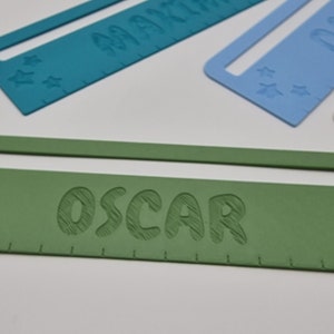 Pode incluir: Uma r&eacute;gua personalizada verde com o nome "OSCAR" em relevo em branco. A r&eacute;gua tem uma pequena janela na parte superior e cinco estrelas brancas no lado esquerdo.