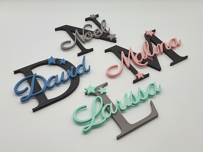 May include: Five wooden names with stars, painted in different colors. The names are David, Noel, Malina, Larissa, and a fifth name that is not visible in the image.