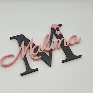 May include: A pink and black wooden name sign with the name "Malina" and two pink stars.