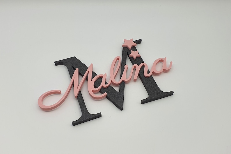 May include: A pink and black wooden name sign with the name "Malina" and two pink stars.