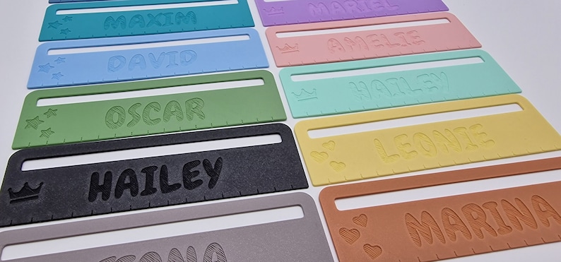 Pode incluir: Um conjunto de r&eacute;guas personalizadas coloridas com diferentes nomes e elementos decorativos. As r&eacute;guas s&atilde;o de pl&aacute;stico e t&ecirc;m um fundo branco. Os nomes s&atilde;o impressos em preto e os elementos decorativos s&atilde;o de diferentes cores. Os nomes nas r&eacute;guas s&atilde;o: Maxim, David, Oscar, Hailey, Amelie, Harley, Leonie, Marina.