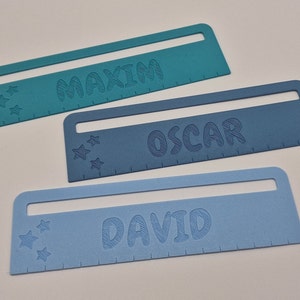 Pode incluir: Tr&ecirc;s r&eacute;guas de pl&aacute;stico azuis com os nomes "Maxim", "Oscar" e "David" impressos nelas. Cada r&eacute;gua tem uma fila de estrelas e uma escala de r&eacute;gua.