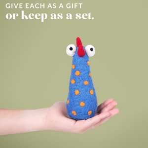 May include: A blue felt toy with orange polka dots and large white eyes. The toy has a red felt beak and is held in a hand.