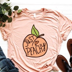 May include: A peach-colored t-shirt with a peach graphic and the text "Just Peachy" in a white outline.