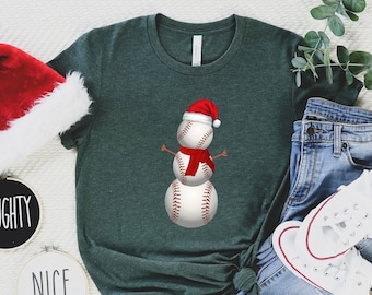 May include: A green t-shirt with a snowman made of baseballs wearing a Santa hat and a red scarf. The snowman is on a white background.