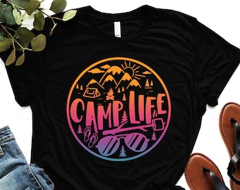 May include: Black t-shirt with a colorful graphic design of a mountain scene with a tent, campfire, sunglasses, and flip-flops. The text "CAMP LIFE" is written in a colorful font.