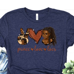 May include: A navy blue t-shirt with a peace sign, heart, and a woman with locs. The design is in copper glitter and the text reads "peace love locs".