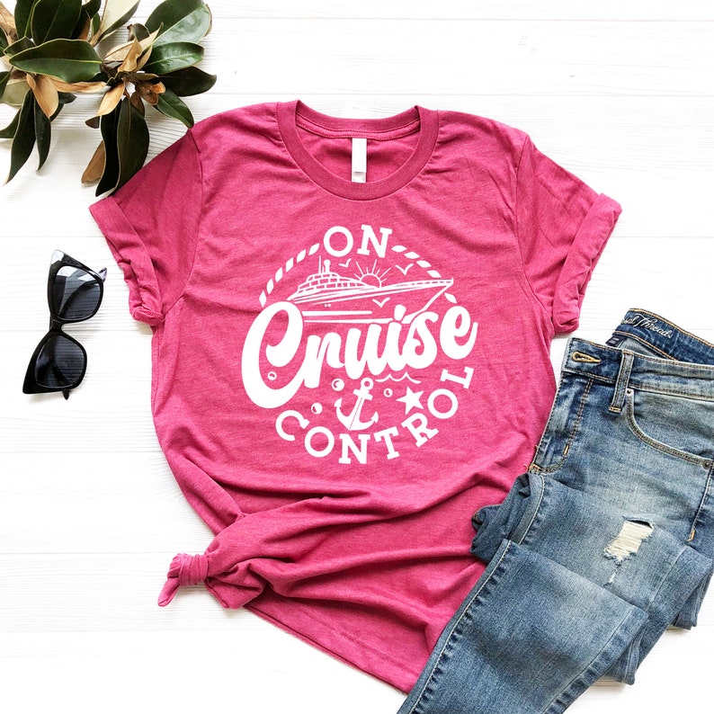 May include: Pink t-shirt with a white graphic design that says "On Cruise Control" with a cruise ship, anchor, and star.