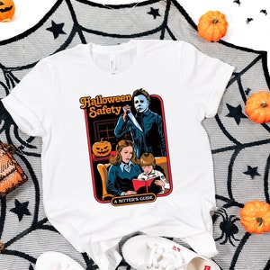 May include: White t-shirt with a graphic of a horror movie character holding a knife, with the text "Halloween Safety A Sitter's Guide" printed on the shirt.