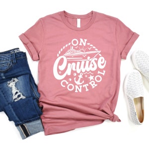 May include: A pink t-shirt with a white graphic design of a cruise ship with the text "On Cruise Control" and a nautical anchor and star.