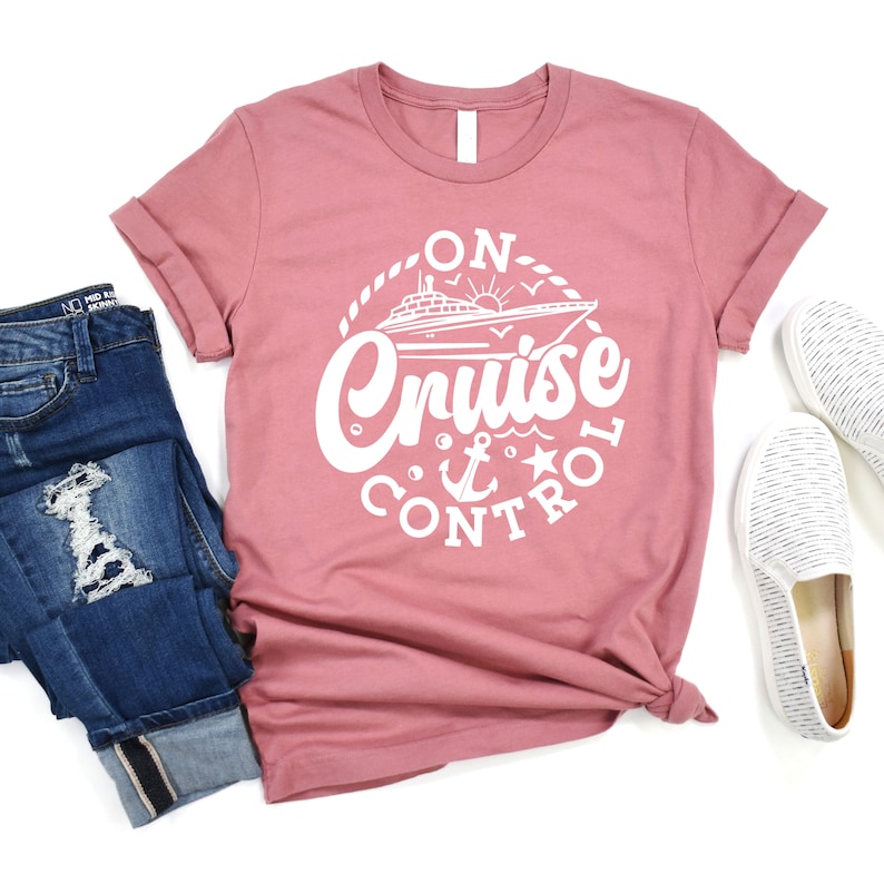 May include: A pink t-shirt with a white graphic design of a cruise ship with the text "On Cruise Control" and a nautical anchor and star.