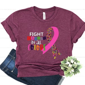 Puede incluir: Una camiseta color granate con el texto "FIGHT CANCER in all COLORS" y una cinta rosa hecha de cintas m&aacute;s peque&ntilde;as de colores.