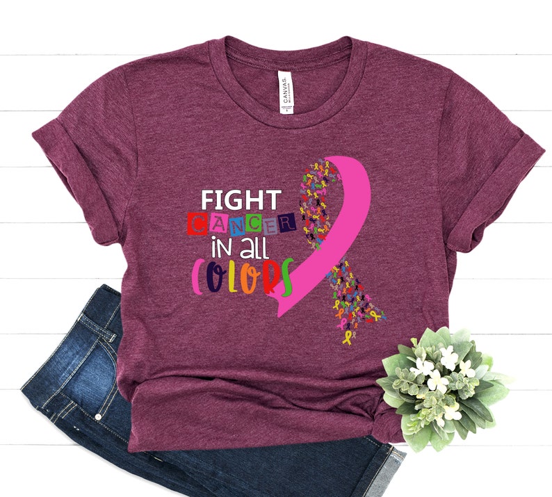Puede incluir: Una camiseta color granate con el texto "FIGHT CANCER in all COLORS" y una cinta rosa hecha de cintas m&aacute;s peque&ntilde;as de colores.
