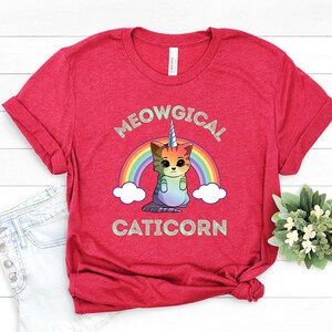 May include: Red t-shirt with a rainbow and a caticorn graphic. The text "MEOWGICAL CATICORN" is printed on the shirt.