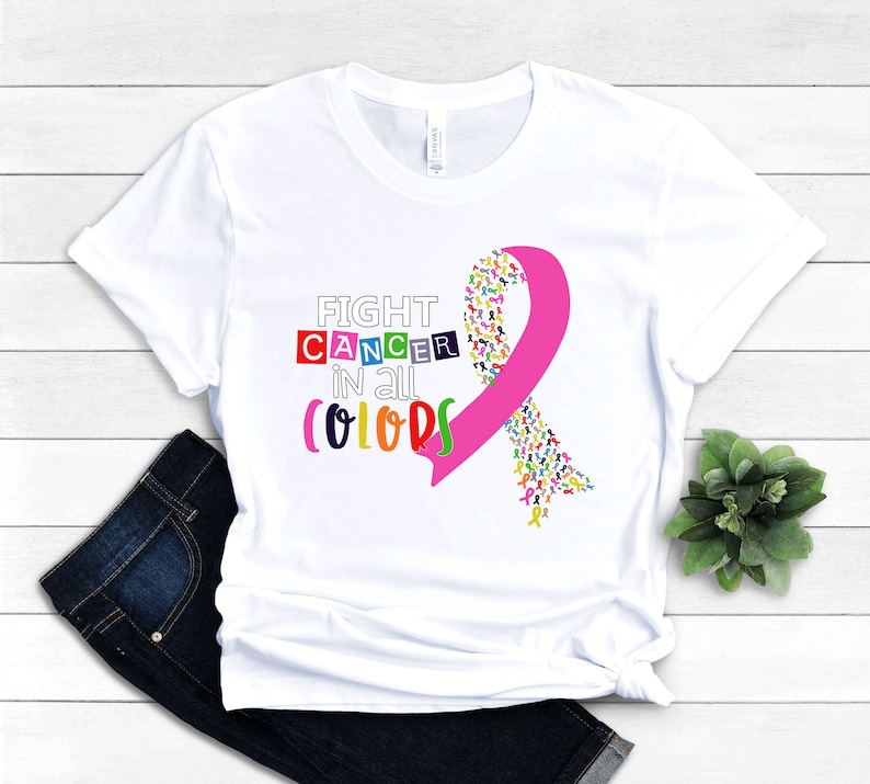 Puede incluir: Camiseta blanca con una cinta rosa hecha de cintas m&aacute;s peque&ntilde;as de colores. El texto "FIGHT CANCER in all COLORS" est&aacute; impreso en la camiseta.