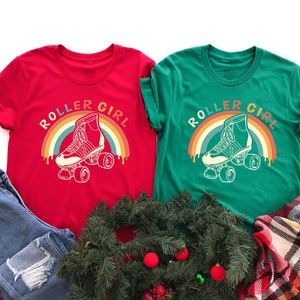 Peut inclure: Deux t-shirts rouge et vert avec le texte "Roller Girl" et un graphique arc-en-ciel avec un patin &agrave; roulettes.