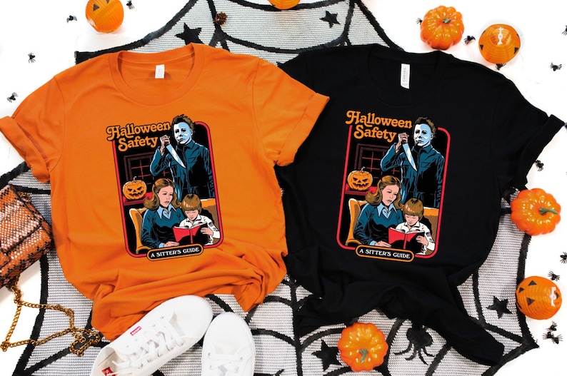 May include: Two t-shirts with a Halloween safety graphic featuring a scary character holding a knife. The graphic is a parody of a children's book cover. The text on the graphic reads "Halloween Safety A Sitter's Guide". One shirt is orange and the other is black.