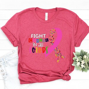 Puede incluir: Camiseta rosa con el texto "FIGHT CANCER in all COLORS" y una cinta rosa hecha de cintas m&aacute;s peque&ntilde;as en varios colores.