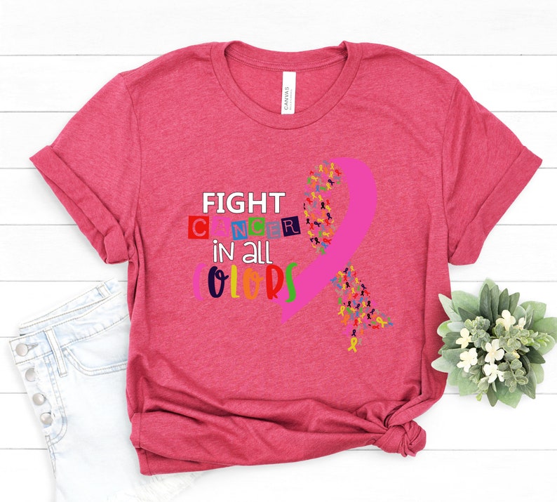 Puede incluir: Camiseta rosa con el texto "FIGHT CANCER in all COLORS" y una cinta rosa hecha de cintas m&aacute;s peque&ntilde;as en varios colores.