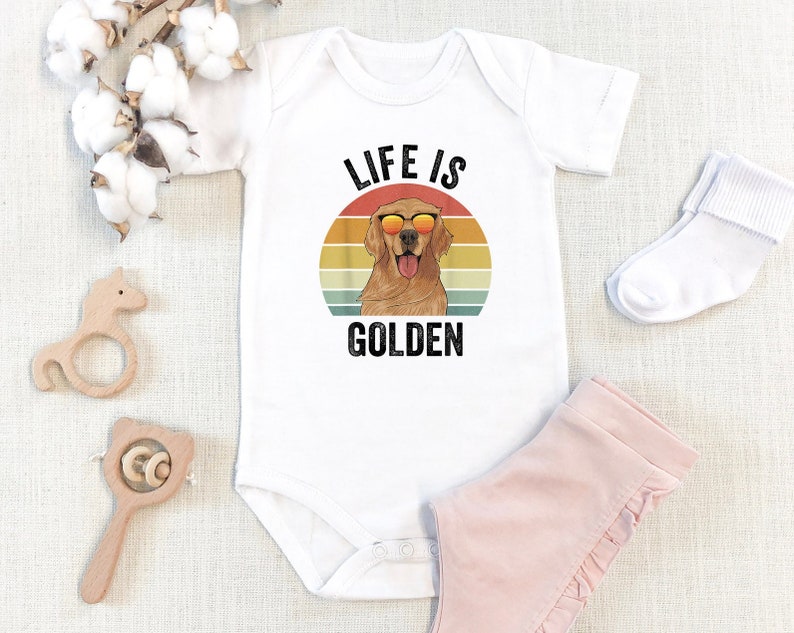 May include: White baby onesie with a retro-style graphic of a golden retriever wearing sunglasses. The graphic says "Life is Golden".